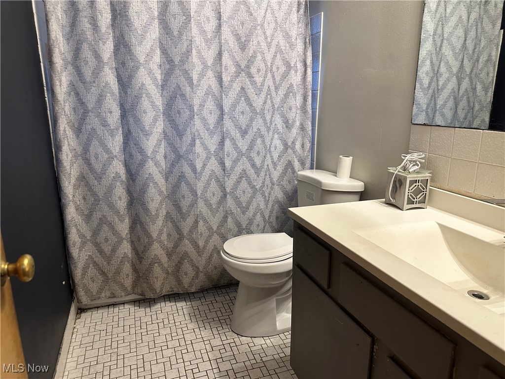 12303 Orme Road Garfield Heights, OH 44125 - Photo 16 of 22 Full bathroom featuring a shower with curtain, toilet, decorative backsplash, and vanity