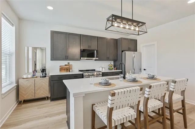 a kitchen with stainless steel appliances a stove a refrigerator a sink dishwasher a dining table and chairs with wooden floor