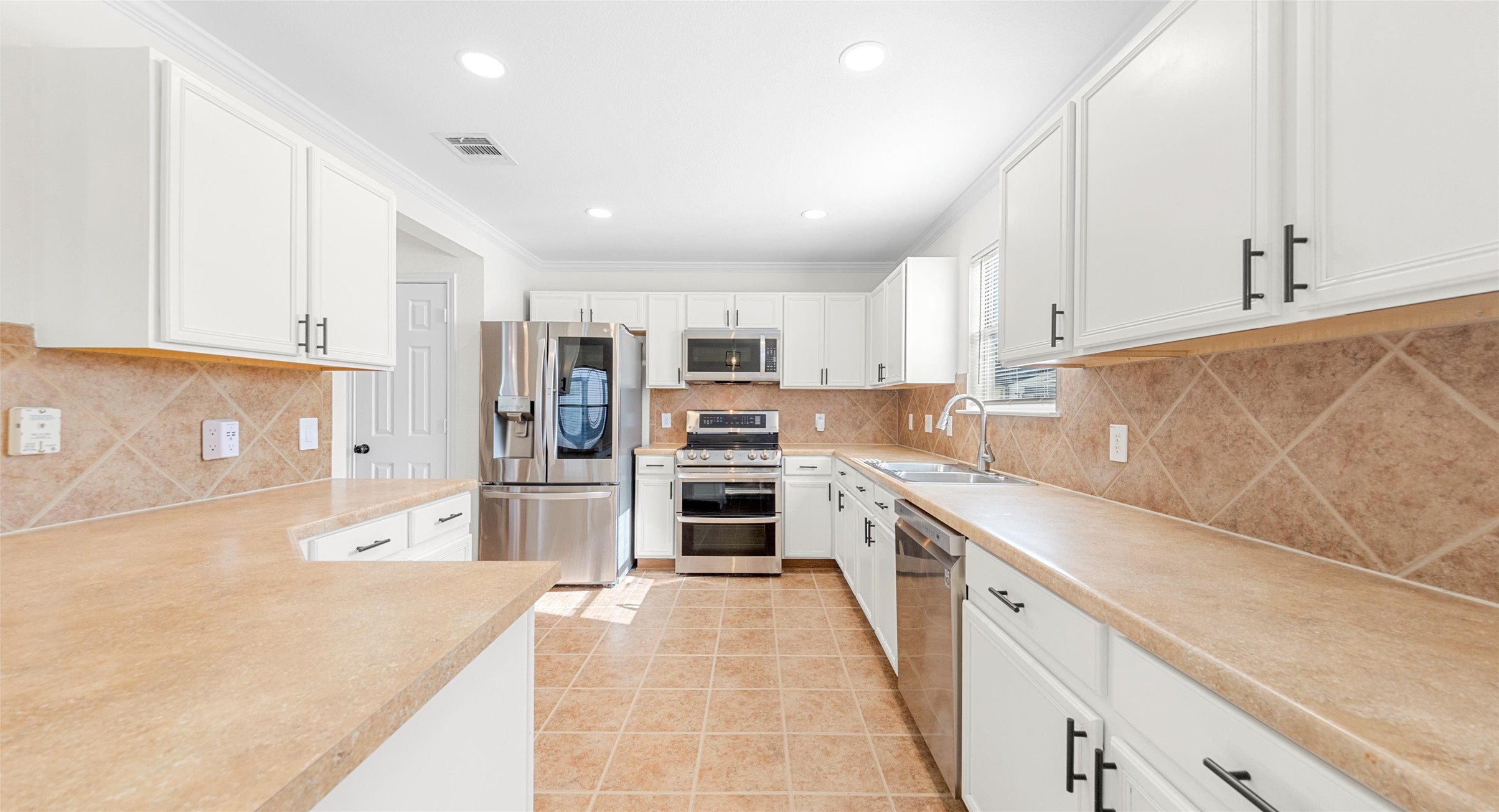 8613 Wiley Way Austin, TX 78747 - Photo 10 of 33 Kitchen with stainless steel appliances, white cabinetry, crown molding, light countertops, and recessed lighting