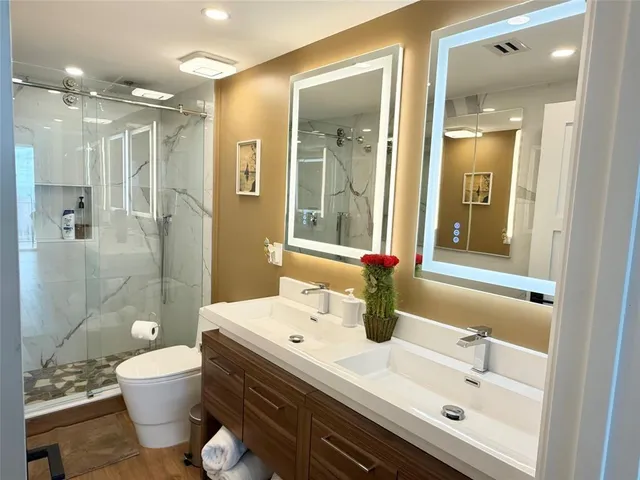 a bathroom with a double vanity sink toilet mirror and shower