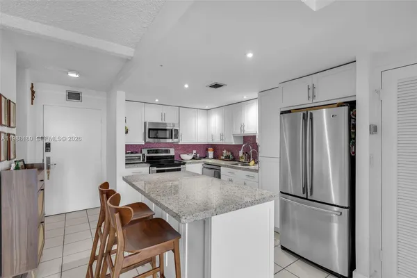 a kitchen with stainless steel appliances kitchen island granite countertop a table chairs and a refrigerator