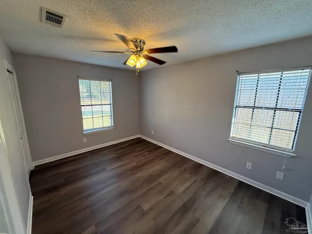 an empty room with wooden floor fan and windows