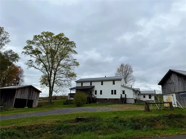 a view of a white house in front of a big yard with plants and large trees