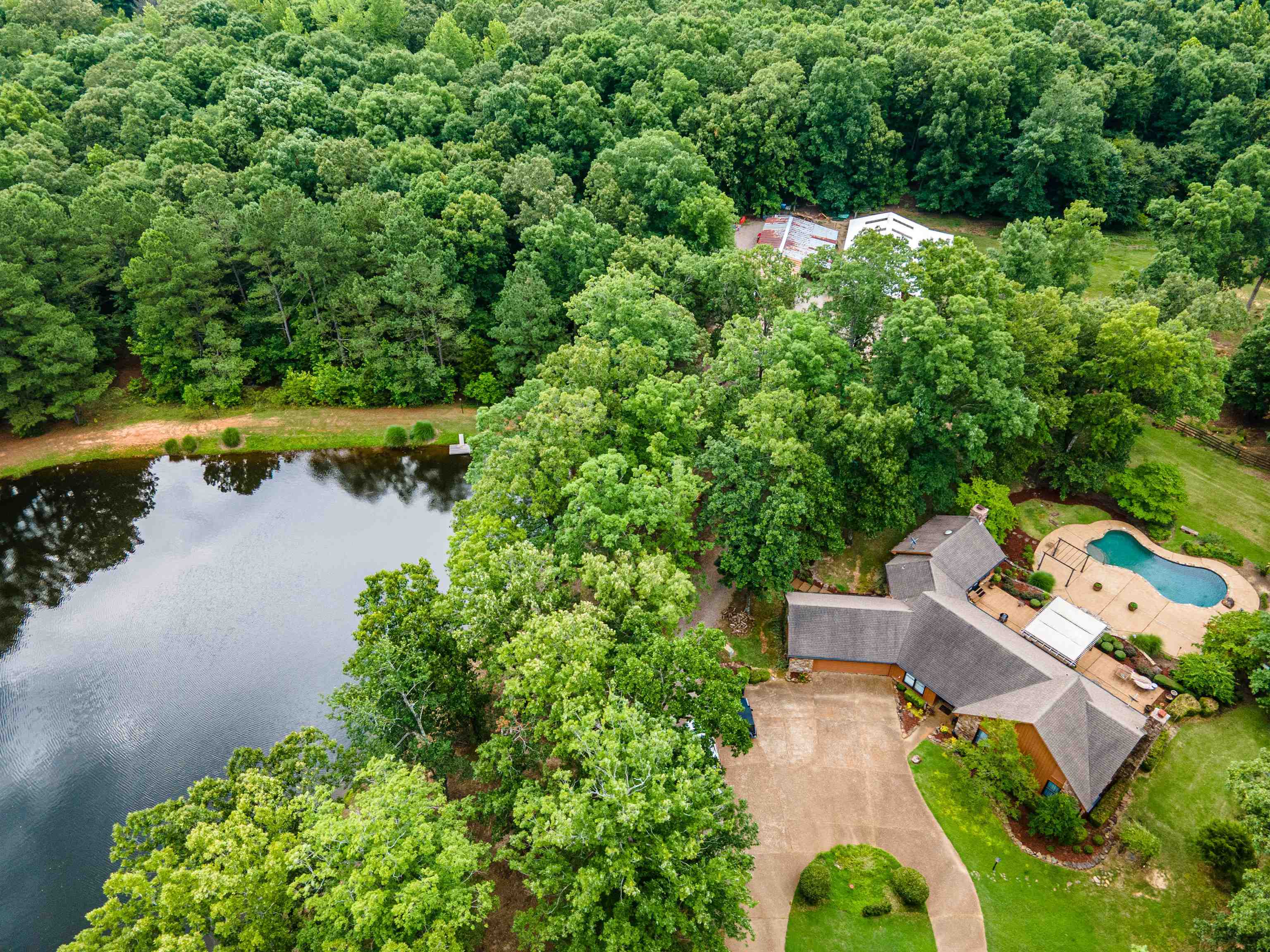 3255 Pittman Road Somerville, TN 38068 - Photo 1 of 35 Expansive property featuring a private pond with a small dock, a custom-shaped swimming pool with surrounding patio, a residential structure with a gray shingle roof, and a paved driveway