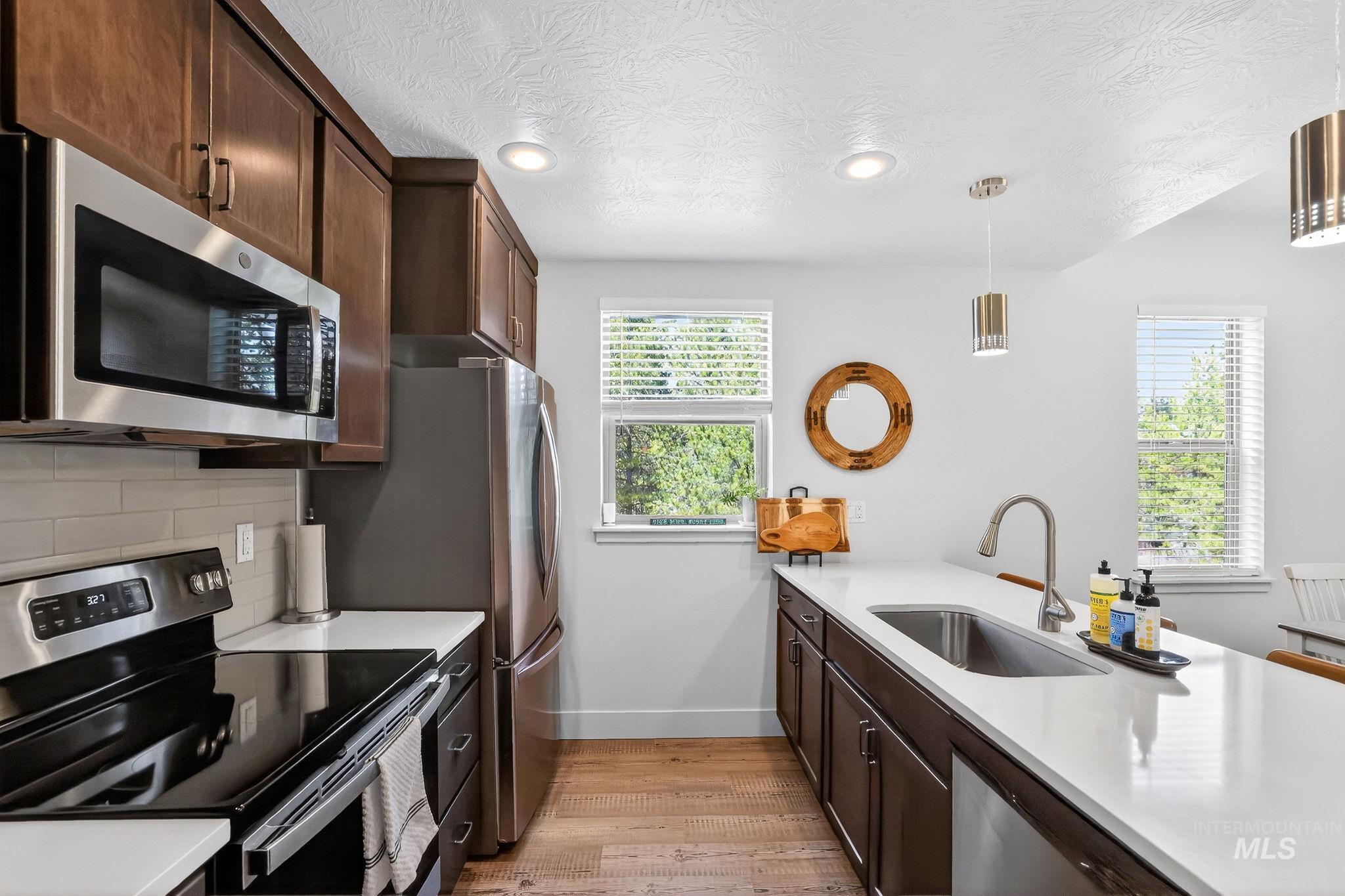 311 Broken Ridge Way McCall, ID 83638 - Photo 11 of 44 Contemporary kitchen featuring stainless steel appliances, dark wood cabinetry, light-toned countertops, wood-finish flooring, and two windows with blinds