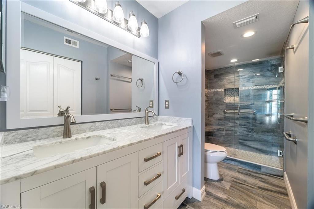 1715 Reuven Circle, Unit 2103 Naples, FL 34112 - Photo 17 of 38 Bathroom with double vanity, a stall shower, wood finished floors, and recessed lighting