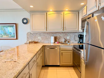 a kitchen with granite countertop a refrigerator a sink and white cabinets