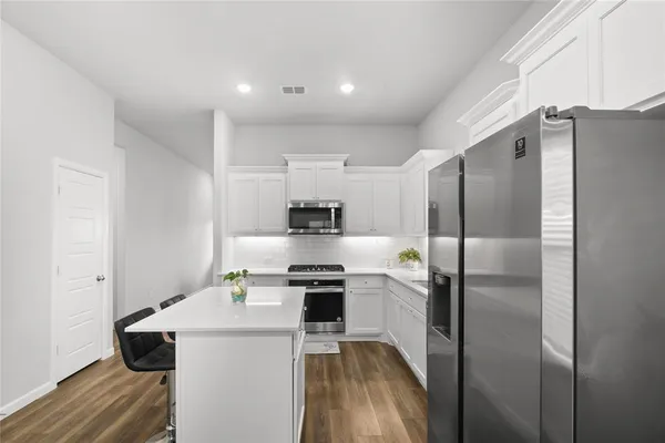 a kitchen with kitchen island a refrigerator a stove a sink dishwasher and white cabinets with wooden floor