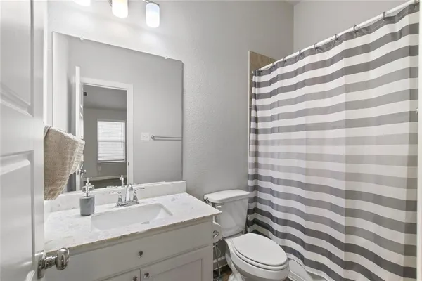 a bathroom with a granite countertop sink a toilet a mirror and shower curtain