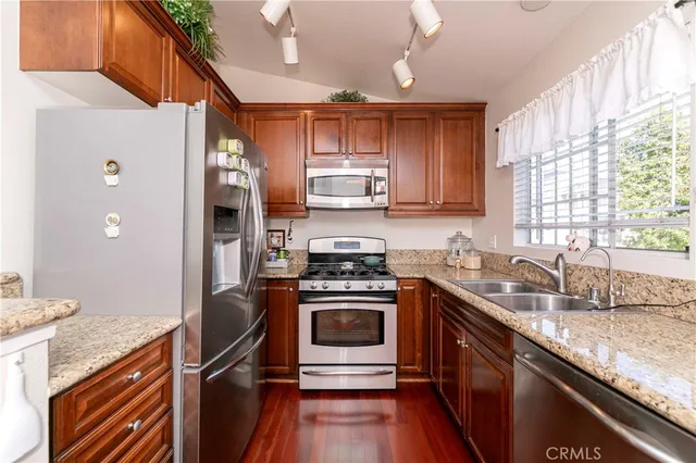 a kitchen with granite countertop a sink cabinets stainless steel appliances and a large window