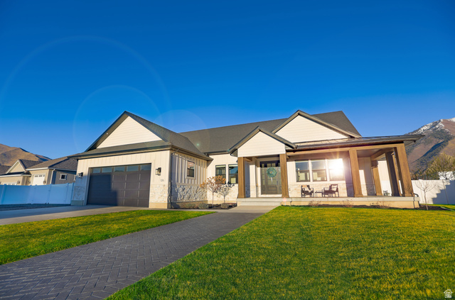Modern farmhouse with stone siding, a porch, concrete driveway, board and batten siding, and an attached garage