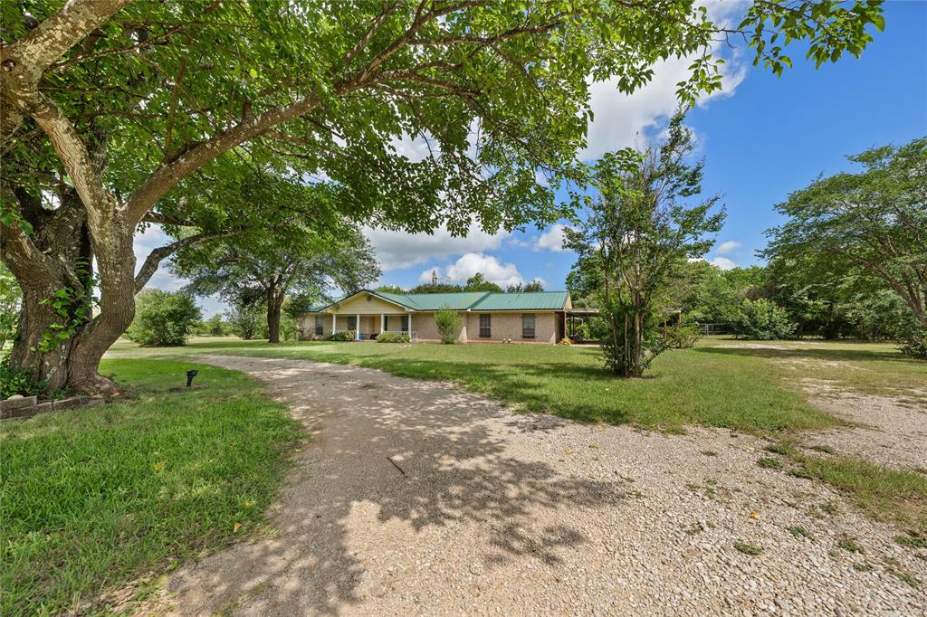 440 Williams Road Lorena, TX 76655 - Photo 18 of 19 Spacious property featuring a gravel driveway, mature trees, and a single-story home with a green metal roof