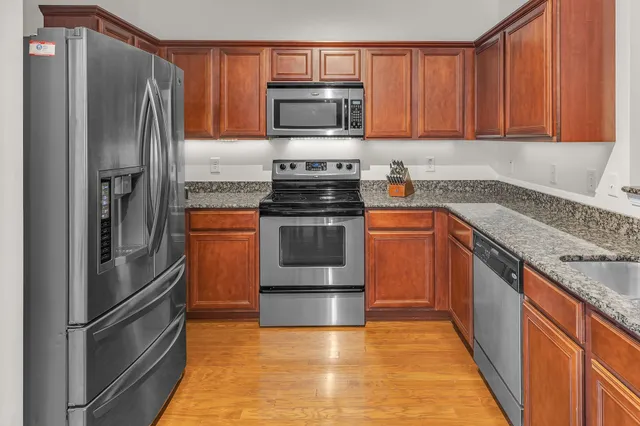 a kitchen with stainless steel appliances granite countertop a refrigerator a stove and a sink with wooden cabinets