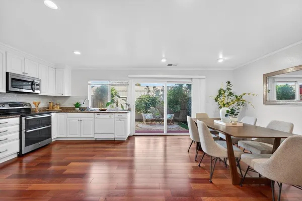 a kitchen with stainless steel appliances granite countertop a stove top oven a refrigerator a dining table and chairs with wooden floor