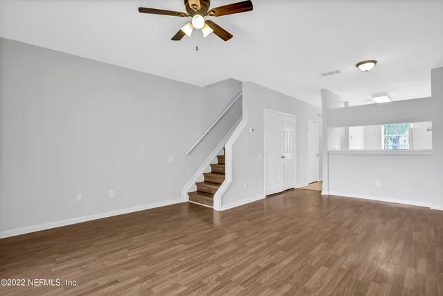 a view of an empty room with wooden floor and a ceiling fan