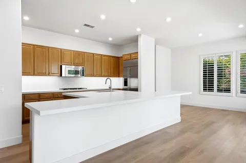 a large kitchen with stainless steel appliances a large counter top a stove a sink a refrigerator and a window