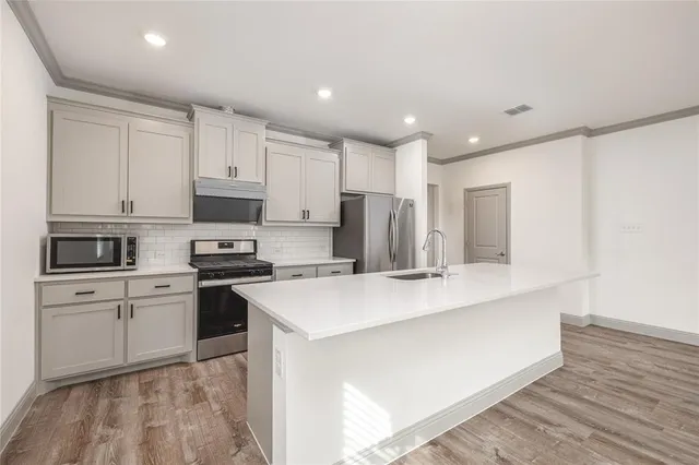 a kitchen with stainless steel appliances a sink a stove a refrigerator cabinets and a window