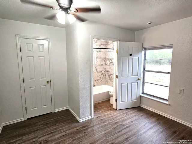 an empty room with wooden floor fan and windows