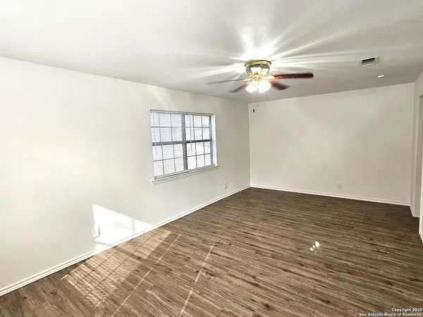 an empty room with wooden floor fan and windows