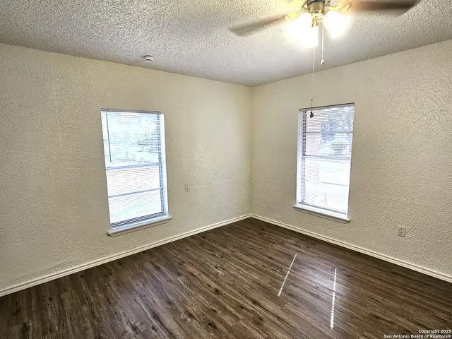 an empty room with wooden floor chandelier fan and windows
