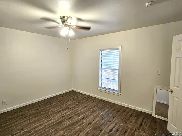 an empty room with wooden floor fan and windows
