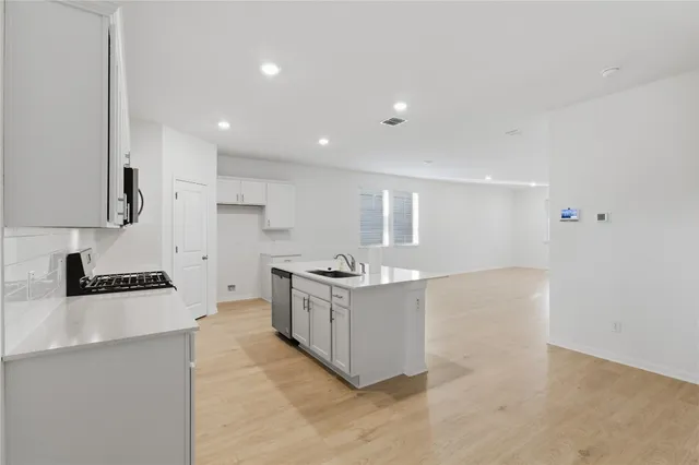 a kitchen with stainless steel appliances granite countertop a stove top oven a sink a refrigerator and white cabinets