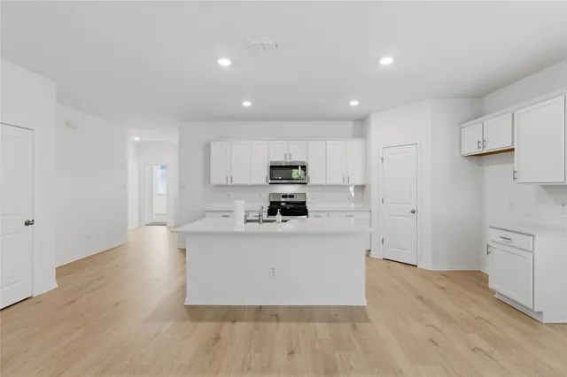 a large kitchen with stainless steel appliances granite countertop a stove a sink a refrigerator and white cabinets with wooden floor