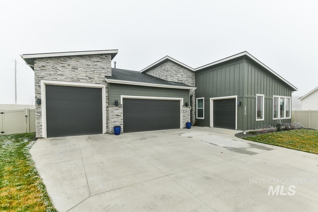 View of front facade featuring board and batten siding, stone siding, a garage, and driveway