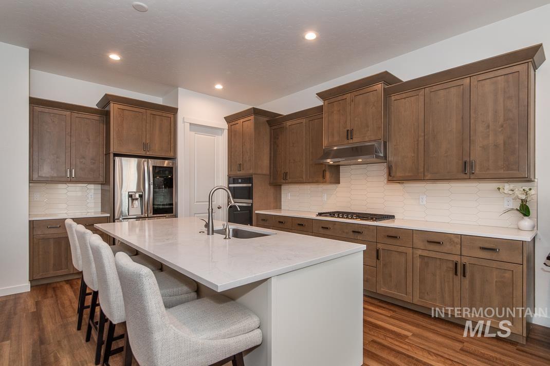 5610 Sparky Avenue Caldwell, ID 83607 - Photo 5 of 14 Kitchen featuring a kitchen breakfast bar, stainless steel appliances, an island with sink, under cabinet range hood, and decorative backsplash