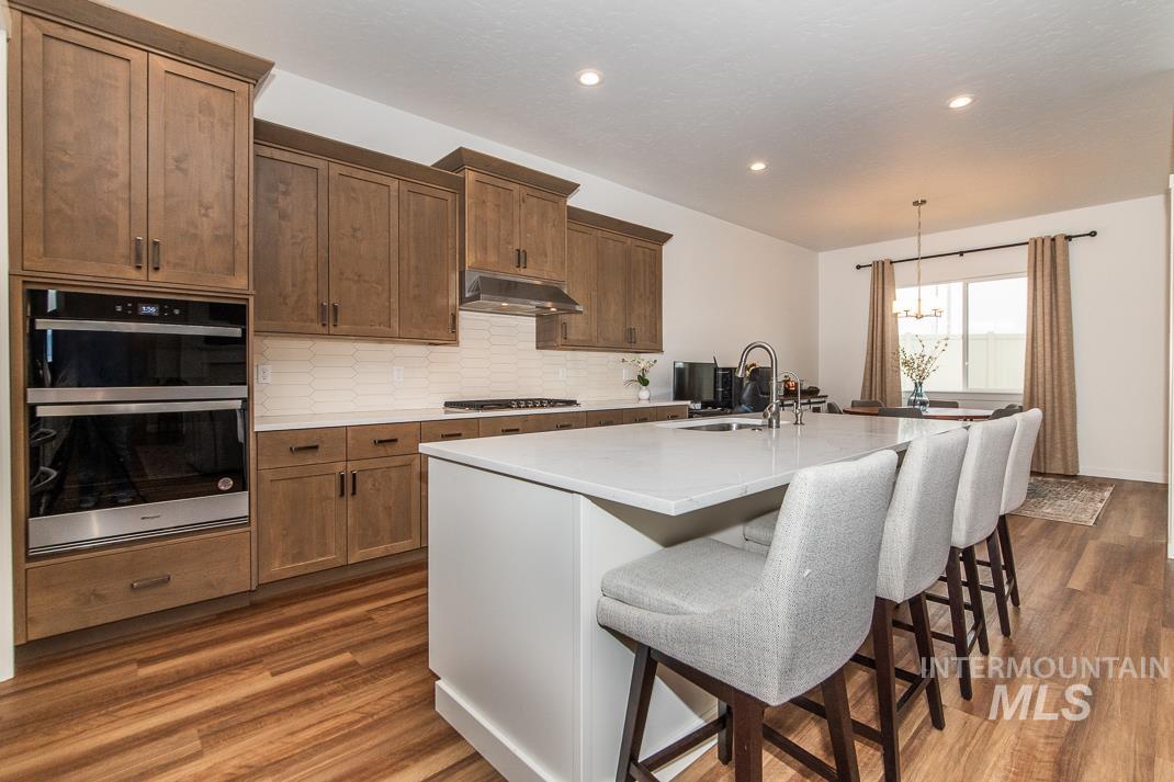 5610 Sparky Avenue Caldwell, ID 83607 - Photo 7 of 14 Kitchen featuring backsplash, appliances with stainless steel finishes, a kitchen breakfast bar, decorative light fixtures, and brown cabinets