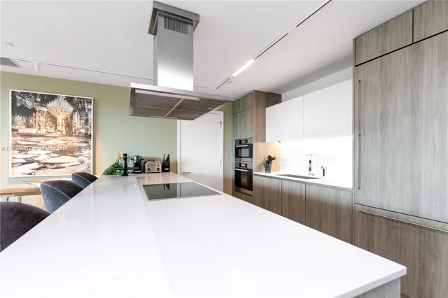 a large white kitchen with kitchen island a large window a sink and stainless steel appliances