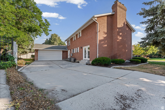 8441 Rua Branco Drive Sandy, UT 84093 - Photo 41 of 47 Brick exterior with a prominent brick chimney, an attached two-car garage, and a concrete driveway