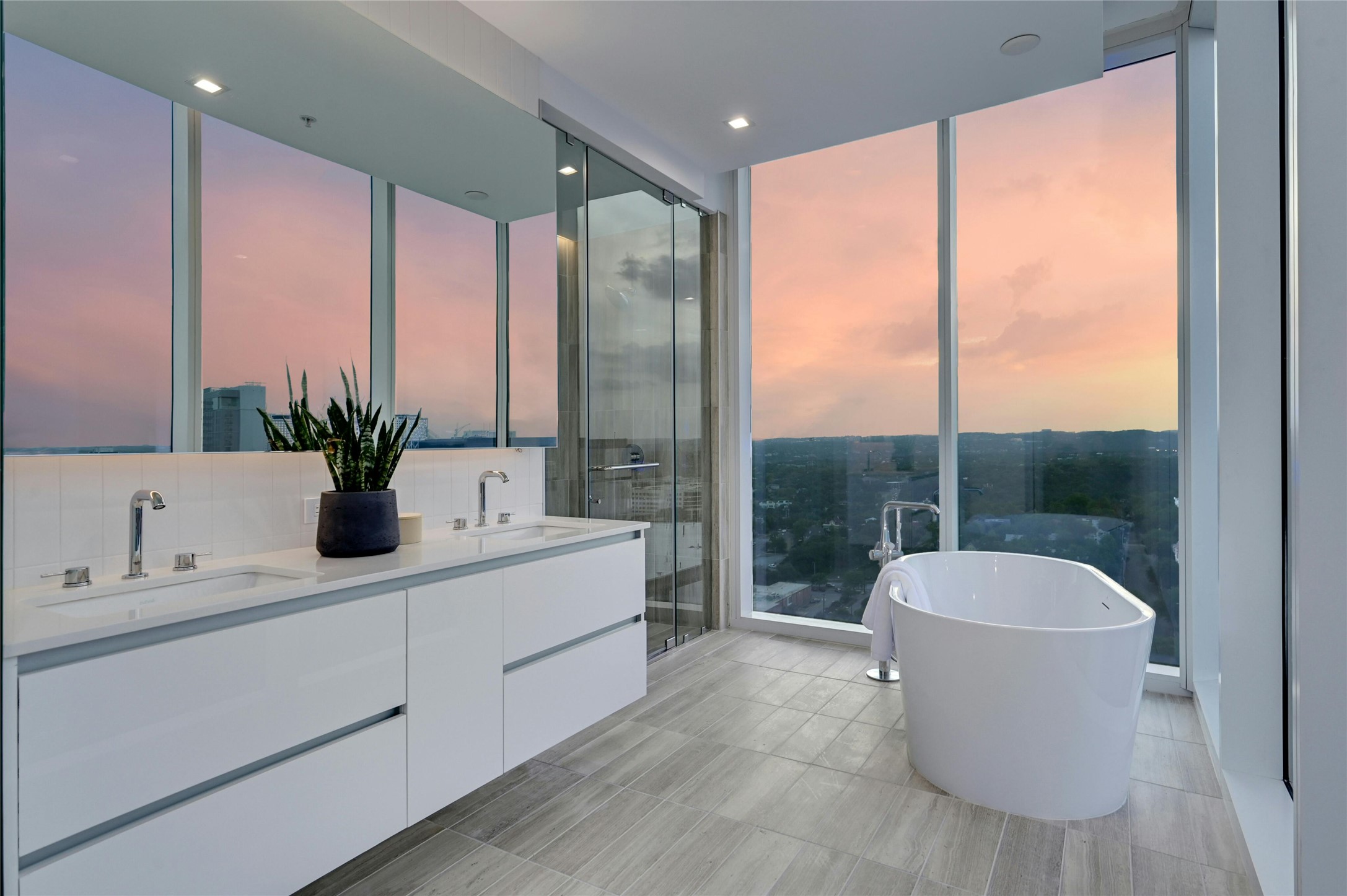 Soak in luxury with breathtaking sunset views from this spa-inspired primary bath. Featuring a freestanding soaking tub, an expansive double vanity with sleek modern cabinetry, and a glass-enclosed walk-in shower, this serene retreat combines elegance with panoramic skyline and Hill Country vistas.