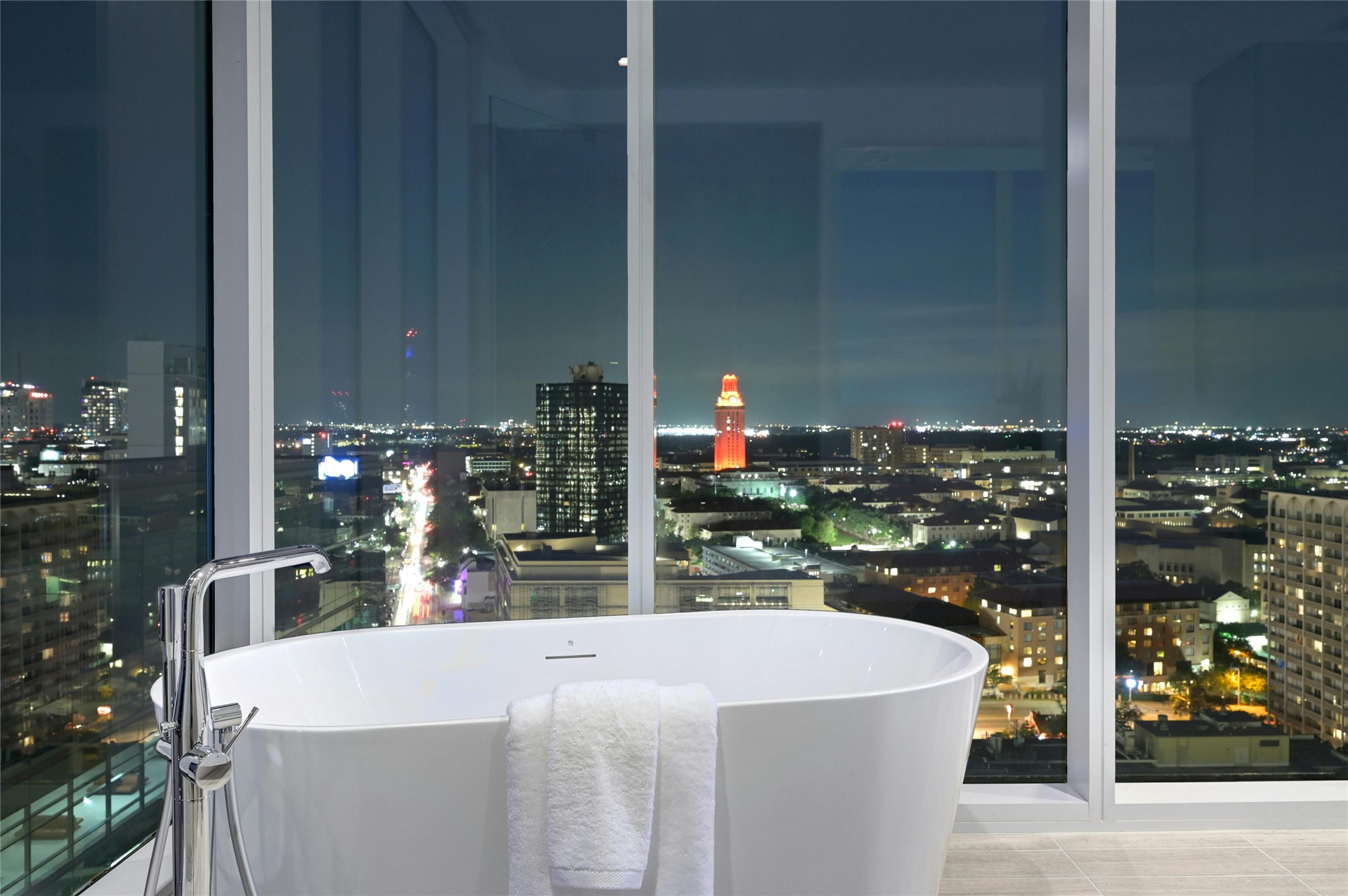 313 West 17th Street, Unit 2204 Austin, TX 78701 - Photo 16 of 40 Spa-inspired primary bathroom with a freestanding soaking tub set against floor-to-ceiling windows, offering dramatic skyline and University Tower views.