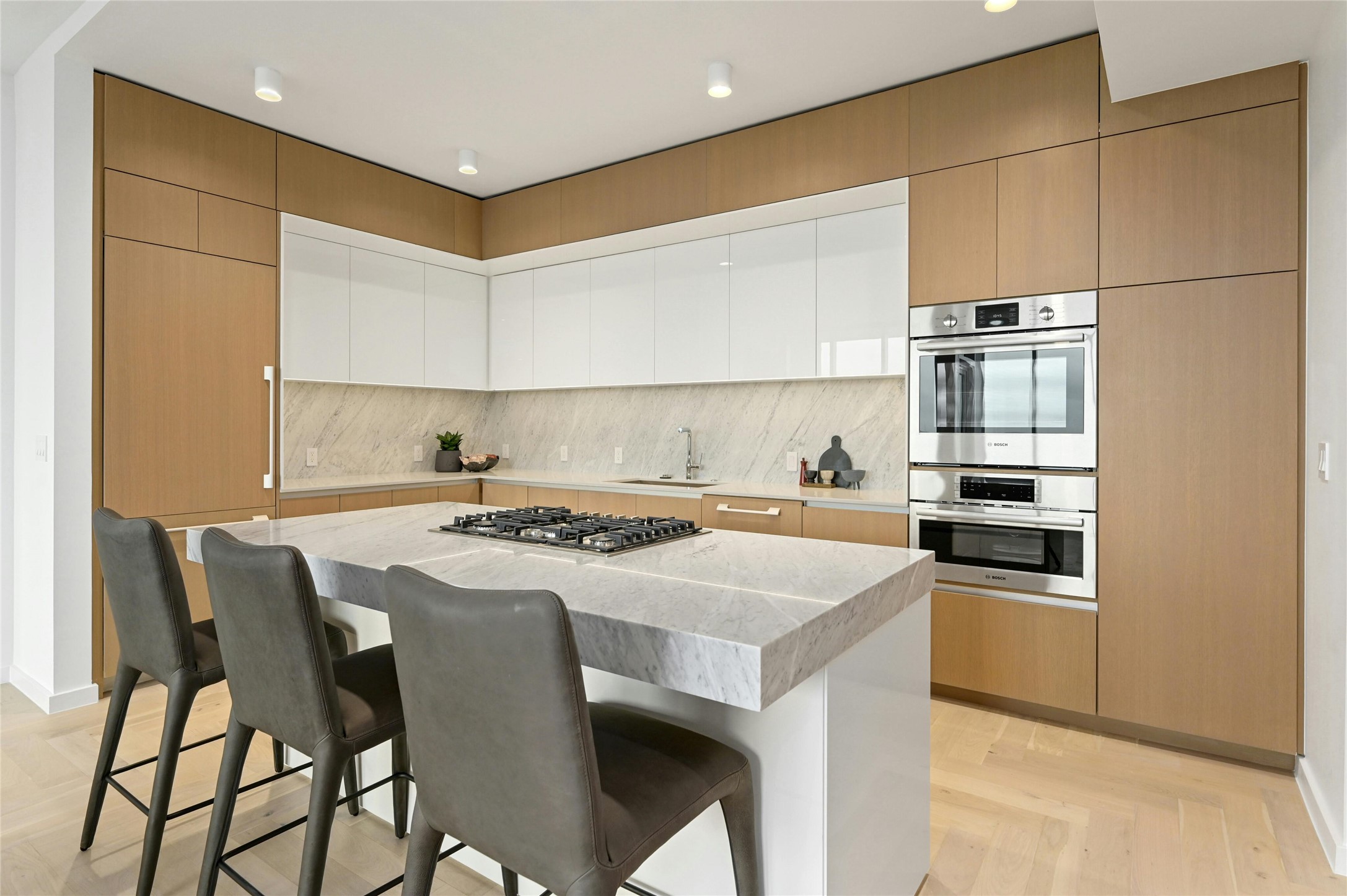 313 West 17th Street, Unit 2204 Austin, TX 78701 - Photo 6 of 40 A modern, open-concept kitchen, dining and living area. The kitchen features a sleek, minimalist design with a large island at its center, topped with white-colored stone countertop. The island includes a built-in gas cooktop and stainless steel oven. Custom cabinetry seamlessly conceals the integrated refrigerator, maintaining clean lines and a refined aesthetic.