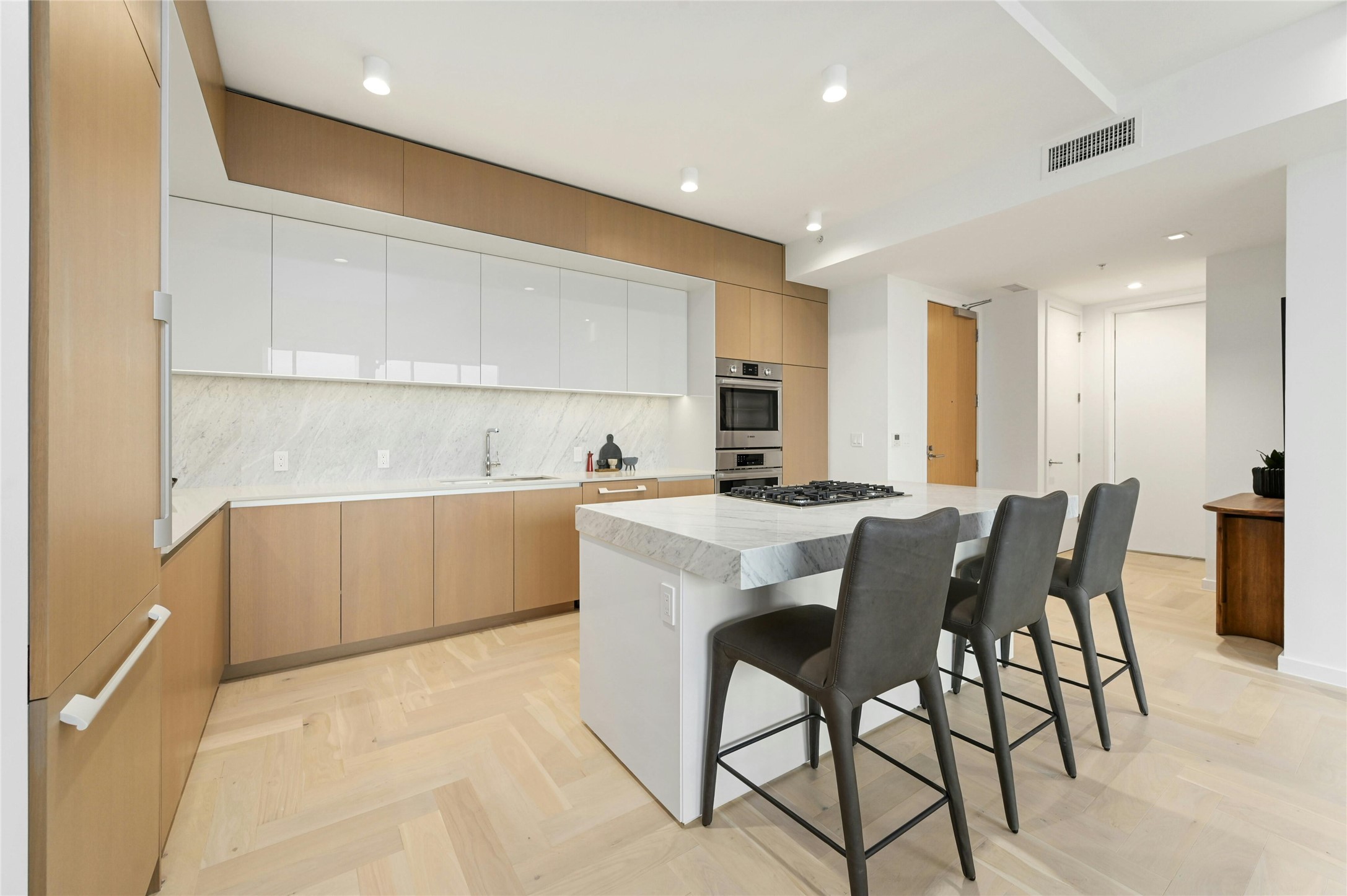 313 West 17th Street, Unit 2204 Austin, TX 78701 - Photo 8 of 40 A modern, open-concept kitchen, dining and living area. The kitchen features a sleek, minimalist design with a large island at its center, topped with white-colored stone countertop. The island includes a built-in gas cooktop and stainless steel oven. Custom cabinetry seamlessly conceals the integrated refrigerator, maintaining clean lines and a refined aesthetic.