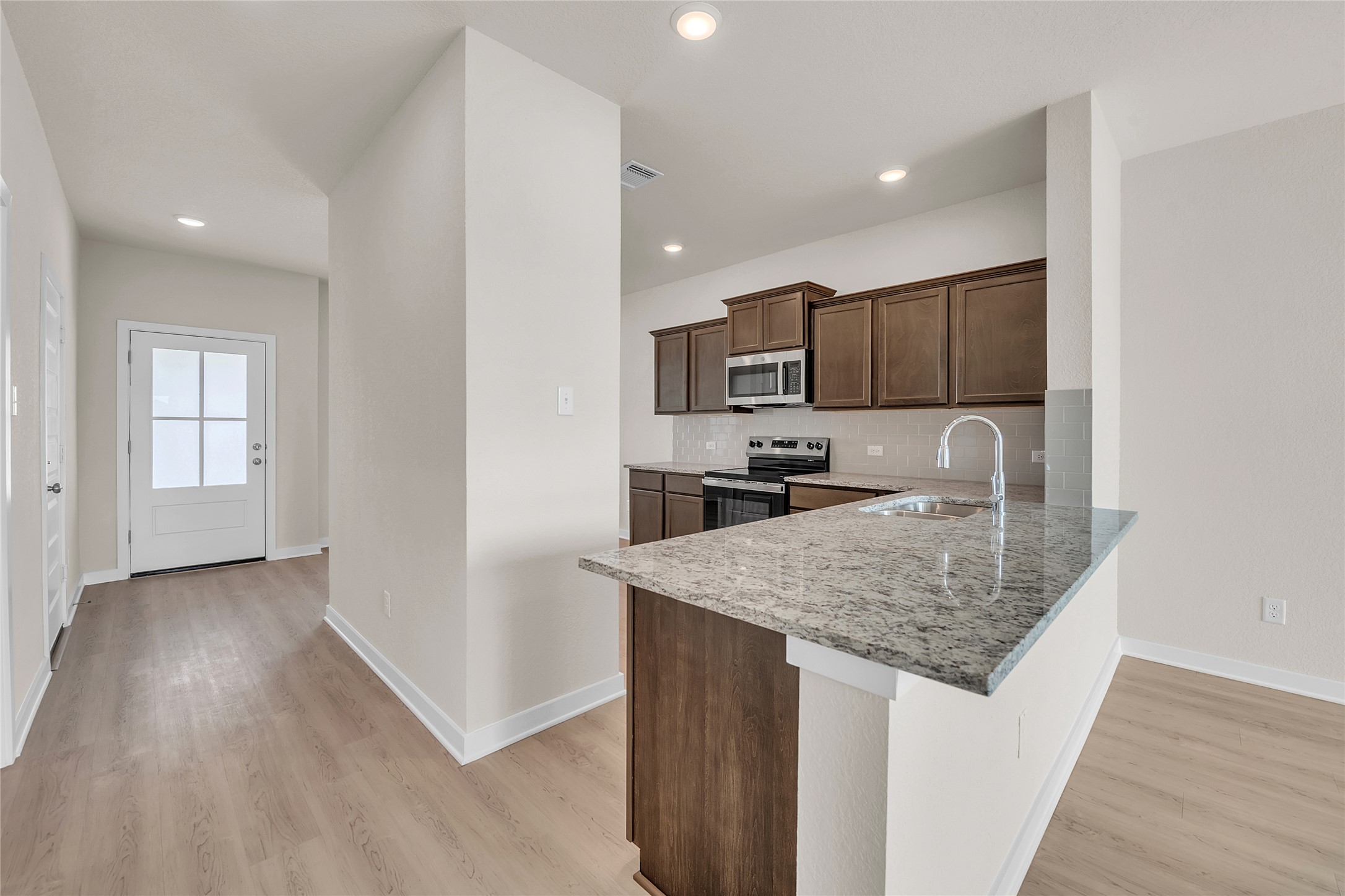 290 Boatright Boulevard Jarrell, TX 76537 - Photo 12 of 32 Kitchen with tasteful backsplash, appliances with stainless steel finishes, light stone countertops, dark brown cabinets, and a peninsula