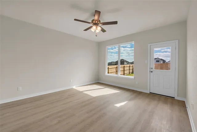 an empty room with wooden floor chandelier fan and windows
