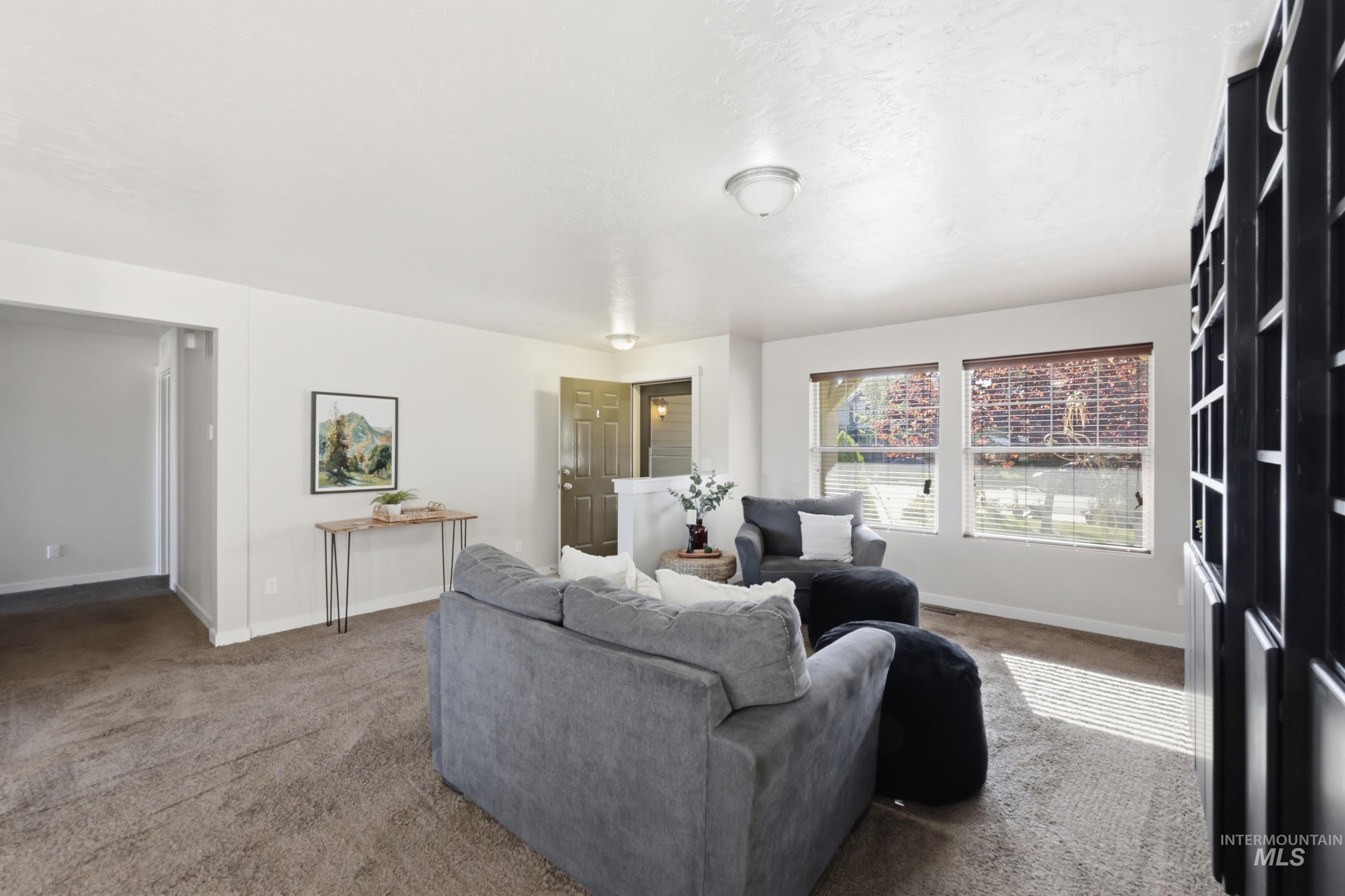 4855 South Chex Way Boise, ID 83709 - Photo 4 of 47 Bright living area featuring neutral carpeting, white walls, multiple windows with blinds, a ceiling-mounted light fixture, and a built-in dark shelving unit