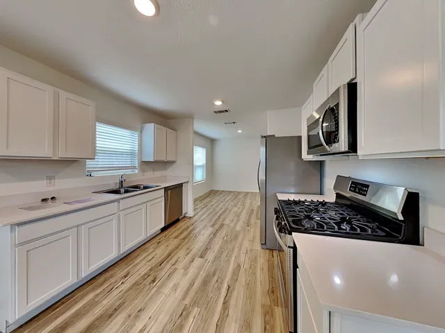 a kitchen with stainless steel appliances a stove a sink a refrigerator white cabinets and wooden floor