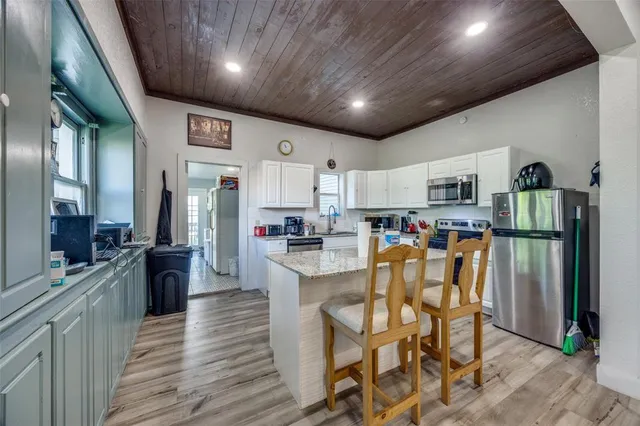 a kitchen with stainless steel appliances a refrigerator a stove top oven a sink dishwasher and white cabinets with wooden floor