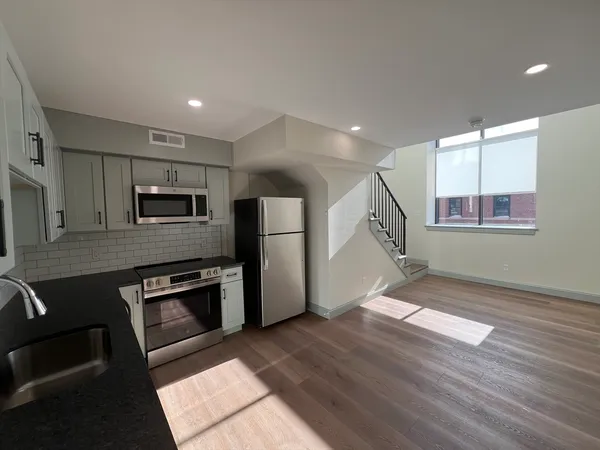a view of empty room with wooden floor and kitchen view