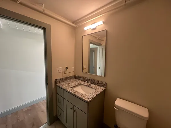a bathroom with a granite countertop toilet a sink and a mirror