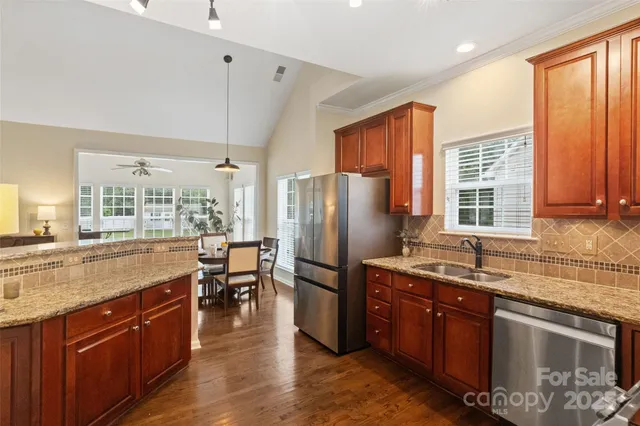 a kitchen with stainless steel appliances granite countertop a refrigerator a sink dishwasher a stove and a dining table with wooden floor