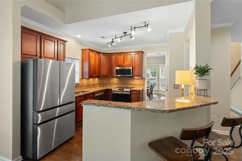 a kitchen with stainless steel appliances granite countertop a refrigerator a sink dishwasher a stove a dining table and chairs with wooden floor