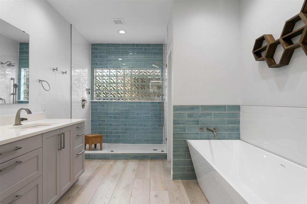 14140 Regency Place Dallas, TX 75254 - Photo 23 of 38 Bathroom featuring a freestanding tub, glass-enclosed shower with glass block accent, single vanity with light grey cabinetry and white countertop, and wood-finish flooring
