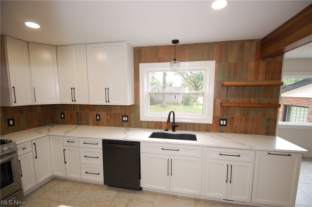 408 Ewing Road Youngstown, OH 44512 - Photo 10 of 31 Kitchen with decorative light fixtures, backsplash, light countertops, black dishwasher, white cabinetry, light tile floors, and stainless steel range oven