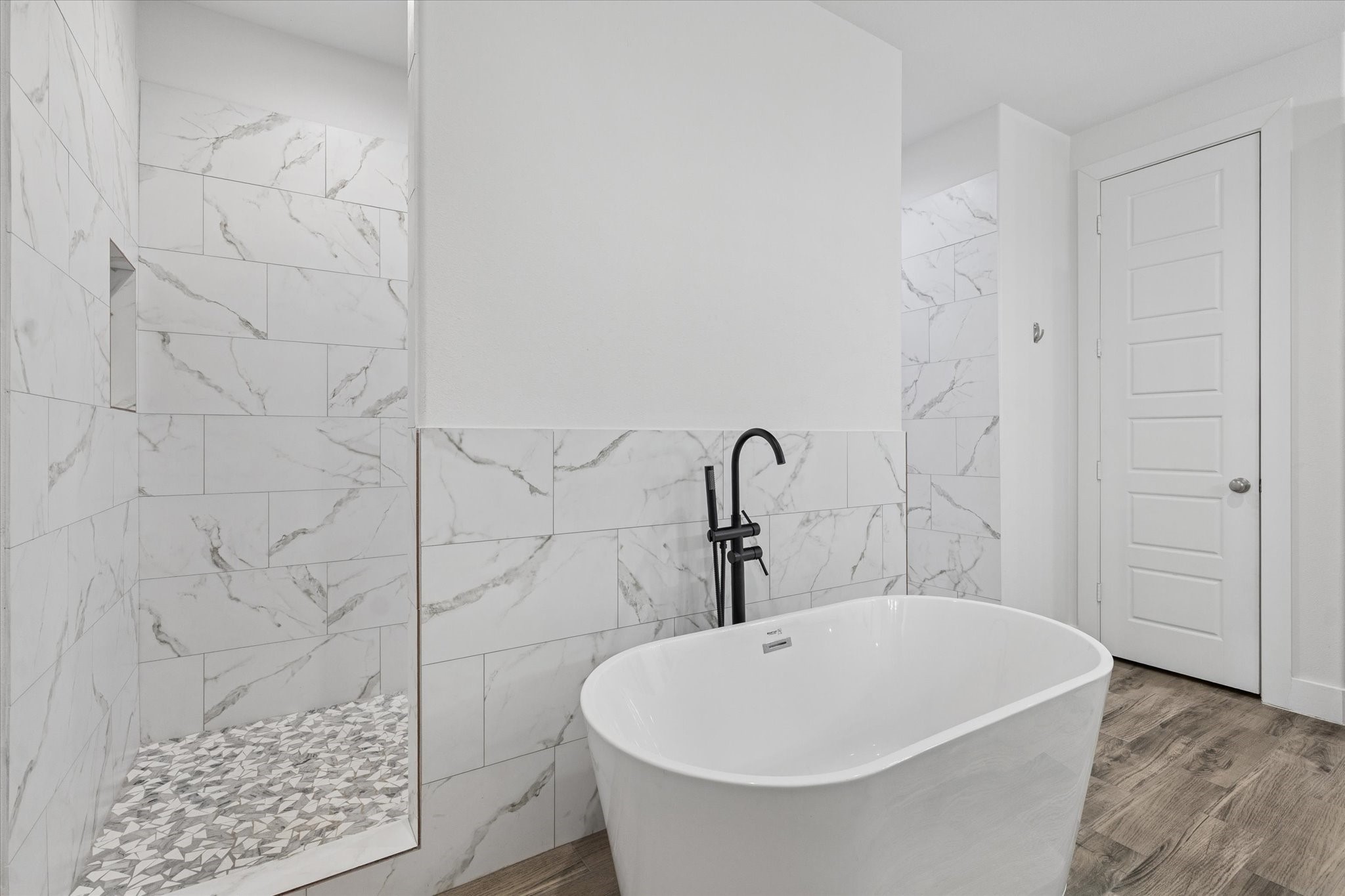 203 Hampton Glen Road Montgomery, TX 77356 - Photo 19 of 35 The elegant and modern bathtub is perfect for relaxing and recharging after a long day. The space showcases sophisticated design details, including wall tile colors that harmonize beautifully with the marble surfaces. The black faucet on the tub provides a striking contrast to the light color palette, while the spacious shower behind the tub and the attention to flooring details complete this unique and visually stunning bathroom. The surfaces are also easy to clean, combining style with functionality.