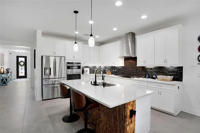 a kitchen with stainless steel appliances kitchen island granite countertop a refrigerator a stove a sink a oven and white cabinets with wooden floor