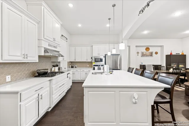 a kitchen with stainless steel appliances kitchen island granite countertop a sink a stove a refrigerator and white cabinets with wooden floor